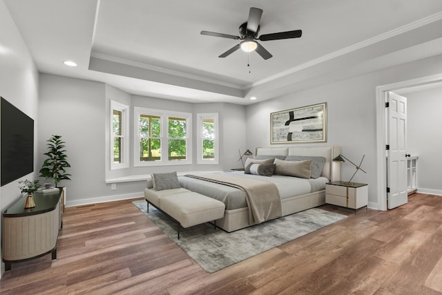 bedroom with ceiling fan, crown molding, wood-type flooring, and a tray ceiling