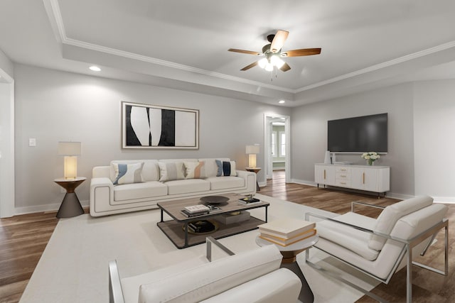 living room featuring hardwood / wood-style flooring, a raised ceiling, ornamental molding, and ceiling fan