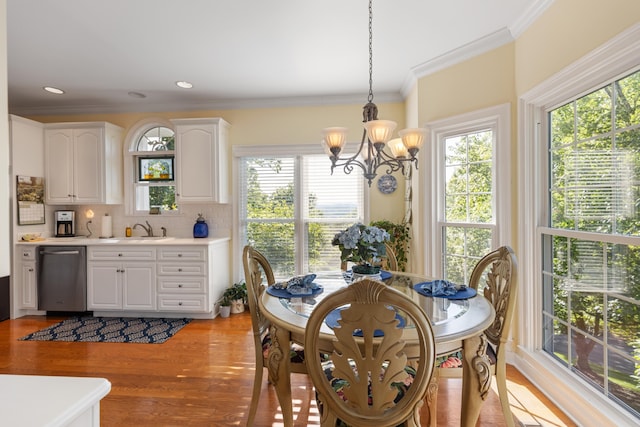 dining space with an inviting chandelier, sink, ornamental molding, and light wood-type flooring