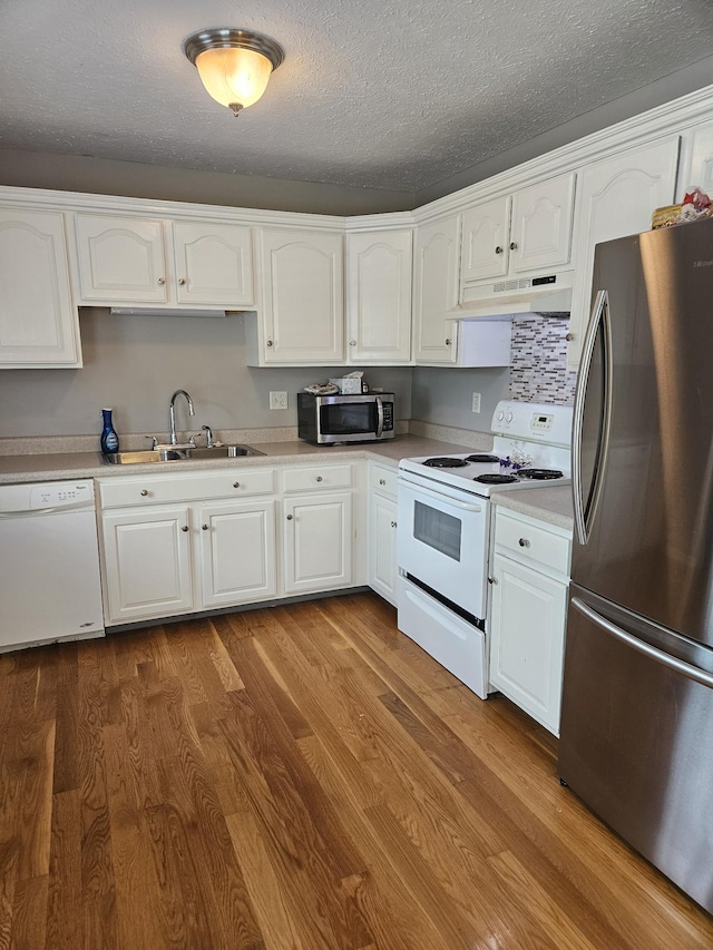 kitchen with under cabinet range hood, stainless steel appliances, white cabinetry, light countertops, and dark wood-style floors