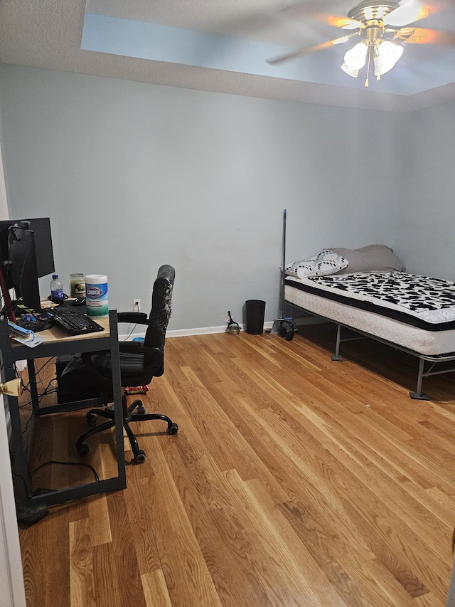 home office featuring a ceiling fan, a textured ceiling, baseboards, and wood finished floors