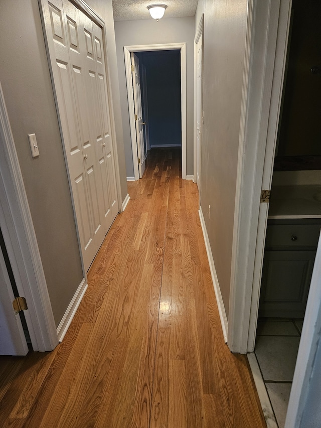 hallway featuring light wood-type flooring and a textured ceiling