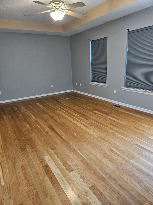 spare room with ceiling fan, wood finished floors, visible vents, and baseboards