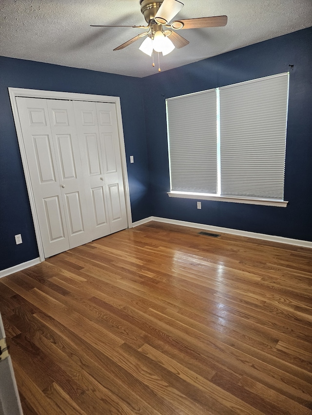 unfurnished bedroom featuring a textured ceiling, dark hardwood / wood-style flooring, a closet, and ceiling fan