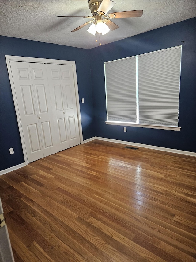 unfurnished bedroom with visible vents, a textured ceiling, baseboards, and wood finished floors