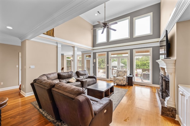 living room with crown molding, a fireplace, light hardwood / wood-style flooring, a high ceiling, and ceiling fan