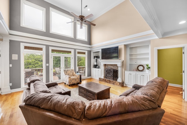 living room featuring a premium fireplace, a towering ceiling, ceiling fan, and light wood-type flooring