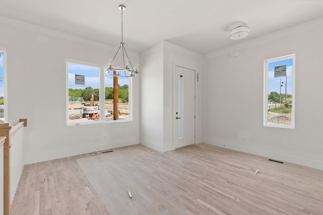 unfurnished dining area with a notable chandelier, a healthy amount of sunlight, and light hardwood / wood-style floors