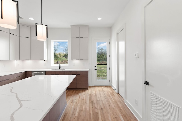 kitchen featuring pendant lighting, sink, light hardwood / wood-style floors, light stone counters, and dark brown cabinetry