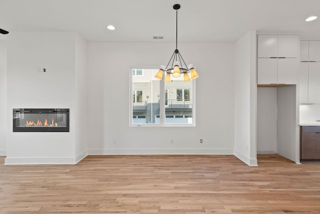 unfurnished dining area with a notable chandelier and light hardwood / wood-style flooring