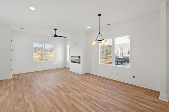 unfurnished living room with ceiling fan with notable chandelier, a healthy amount of sunlight, and light hardwood / wood-style flooring