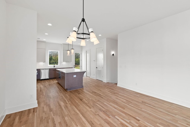 kitchen featuring hanging light fixtures, stainless steel dishwasher, light wood-type flooring, a kitchen island, and a chandelier