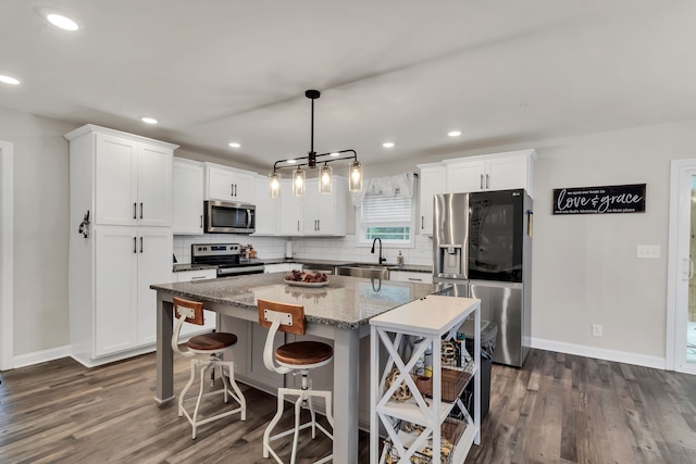 kitchen featuring light stone countertops, a center island, stainless steel appliances, hanging light fixtures, and dark hardwood / wood-style floors