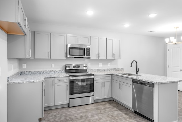 kitchen with a sink, appliances with stainless steel finishes, a peninsula, light wood finished floors, and light stone countertops