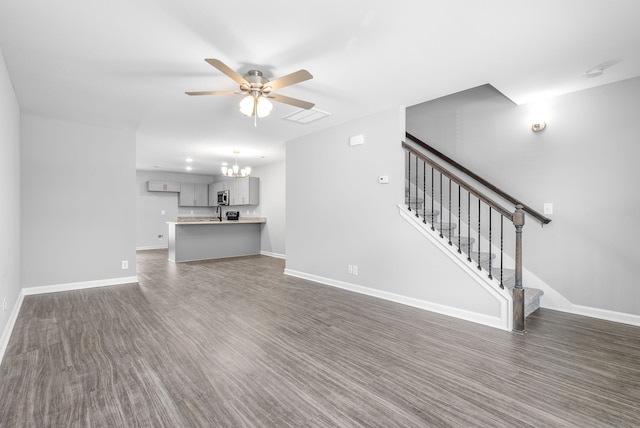 unfurnished living room featuring visible vents, ceiling fan with notable chandelier, dark wood-style floors, baseboards, and stairs