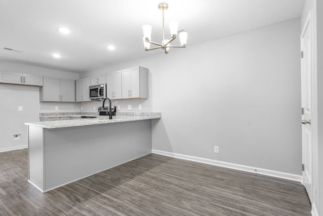 kitchen featuring a chandelier, appliances with stainless steel finishes, kitchen peninsula, light stone countertops, and dark hardwood / wood-style flooring