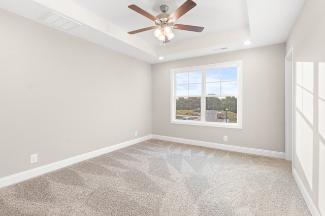 spare room with a tray ceiling, ceiling fan, and carpet