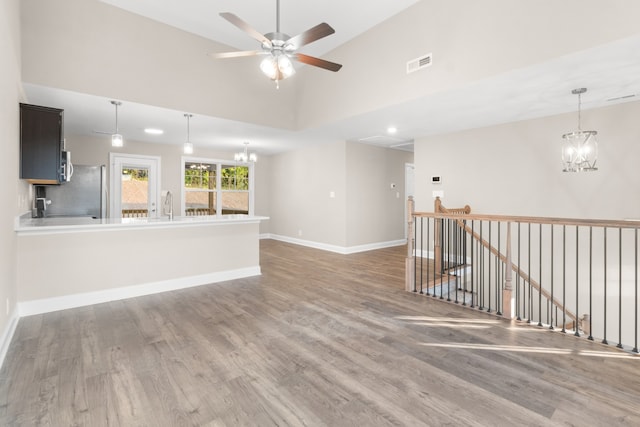 unfurnished living room featuring ceiling fan with notable chandelier, hardwood / wood-style flooring, and high vaulted ceiling