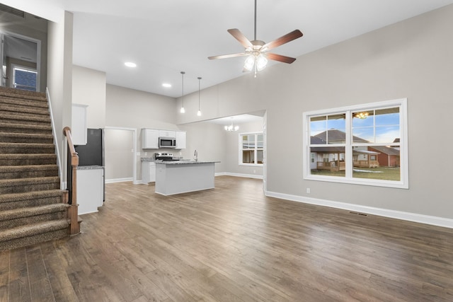 unfurnished living room with a towering ceiling, sink, ceiling fan with notable chandelier, and hardwood / wood-style floors