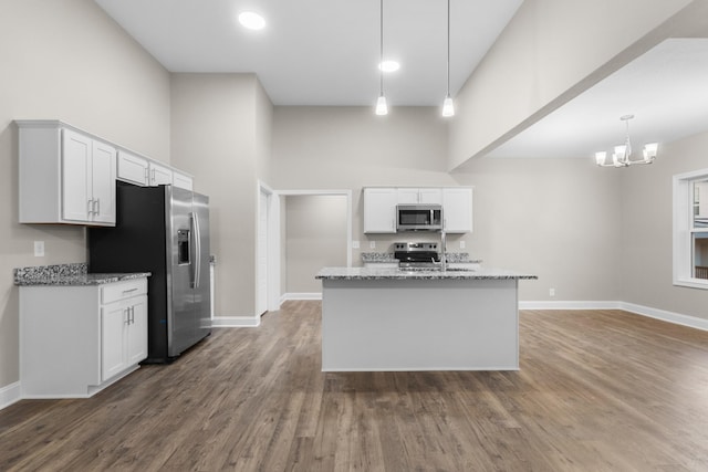 kitchen featuring stainless steel appliances, white cabinetry, light stone counters, and decorative light fixtures