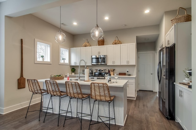 kitchen with dark hardwood / wood-style floors, an island with sink, pendant lighting, white cabinets, and appliances with stainless steel finishes