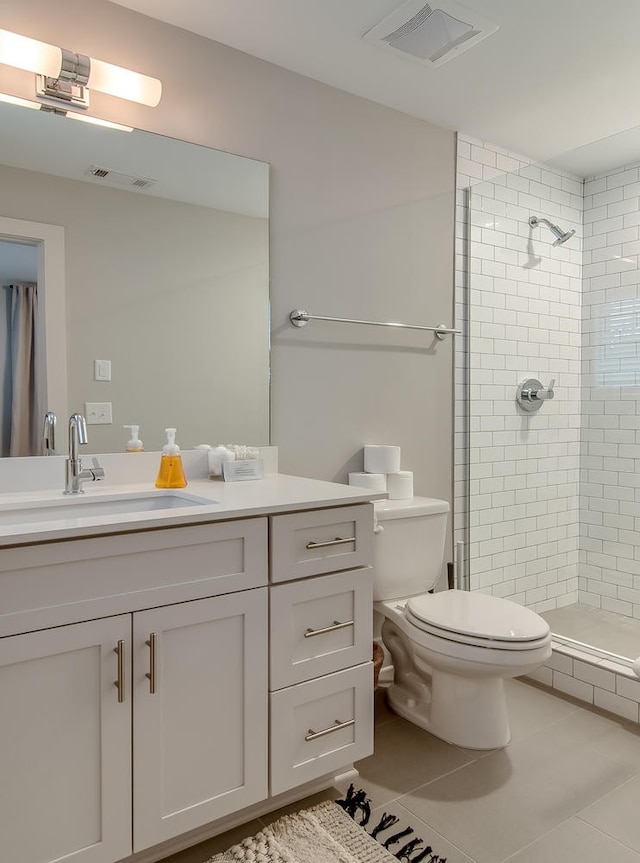 bathroom featuring a tile shower, vanity, toilet, and tile floors