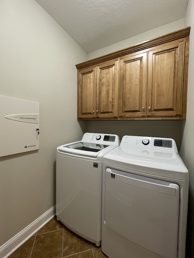 clothes washing area with cabinets, dark tile patterned floors, a textured ceiling, and washing machine and clothes dryer