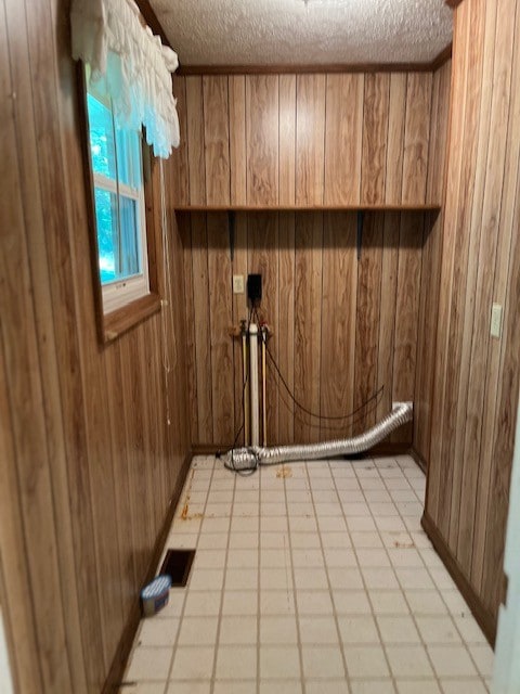 laundry area featuring wooden walls, a textured ceiling, and light tile patterned flooring