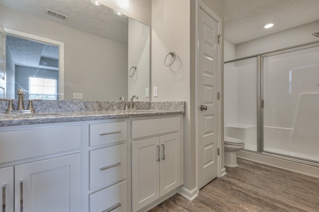 bathroom featuring hardwood / wood-style floors, walk in shower, a textured ceiling, dual bowl vanity, and toilet