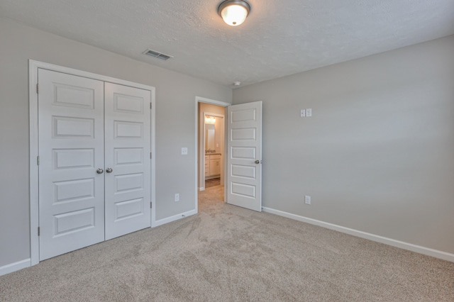 unfurnished bedroom with a textured ceiling, a closet, and light colored carpet