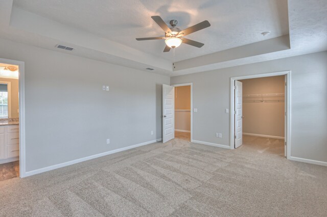 unfurnished bedroom featuring light colored carpet, a walk in closet, ceiling fan, and a raised ceiling