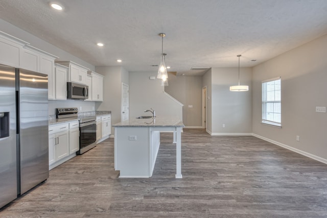 kitchen with stainless steel appliances, an island with sink, white cabinets, wood-type flooring, and pendant lighting