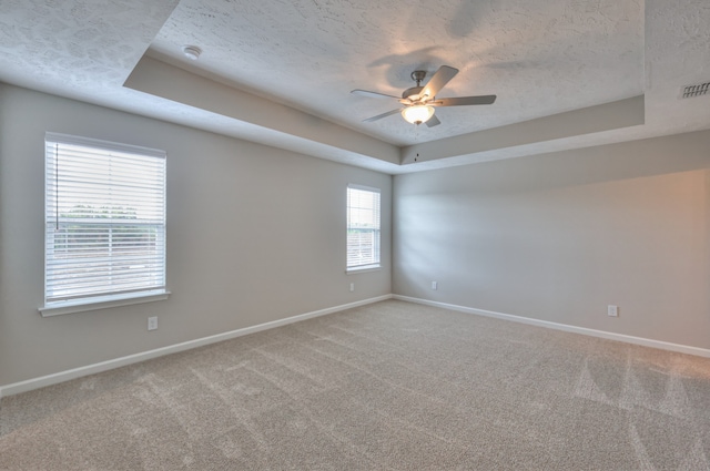 carpeted empty room with a textured ceiling, ceiling fan, and a raised ceiling