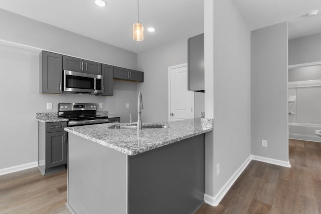 kitchen with appliances with stainless steel finishes, sink, gray cabinetry, hanging light fixtures, and light stone countertops