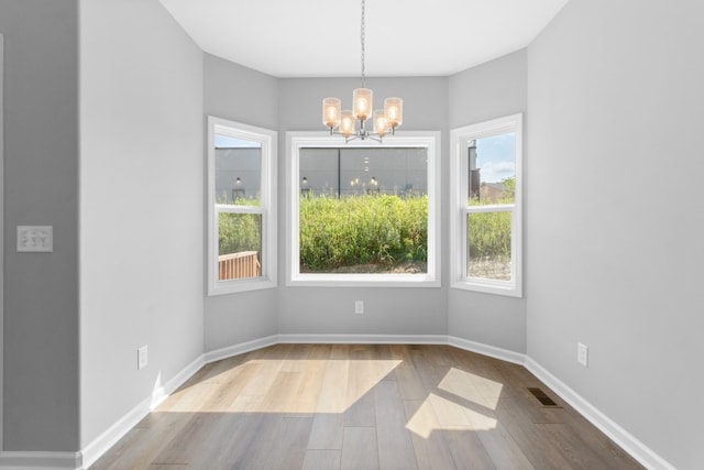 unfurnished dining area featuring a healthy amount of sunlight, a chandelier, and light hardwood / wood-style floors