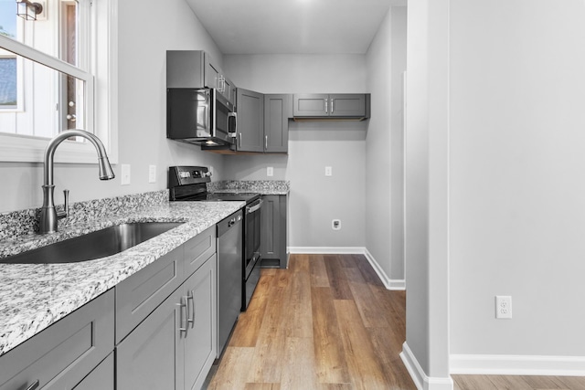 kitchen featuring sink, gray cabinets, stainless steel appliances, light stone countertops, and light hardwood / wood-style floors