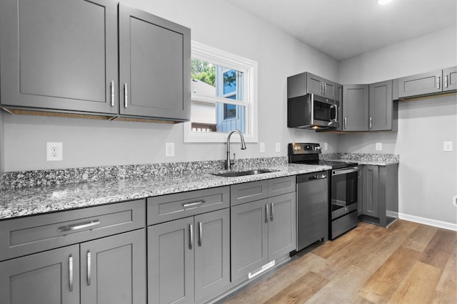 kitchen featuring gray cabinetry, sink, light stone countertops, and appliances with stainless steel finishes