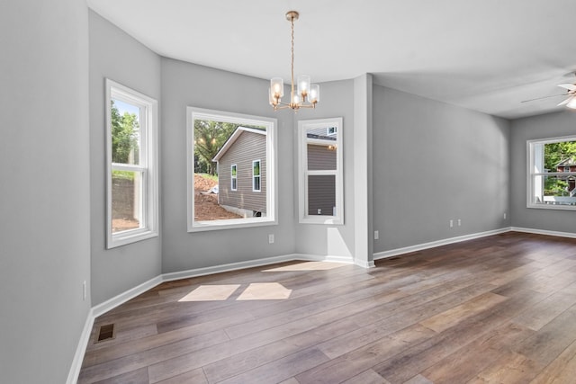 unfurnished dining area with hardwood / wood-style floors, a healthy amount of sunlight, and ceiling fan with notable chandelier