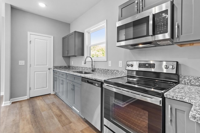 kitchen featuring sink, gray cabinetry, light stone counters, light hardwood / wood-style flooring, and appliances with stainless steel finishes