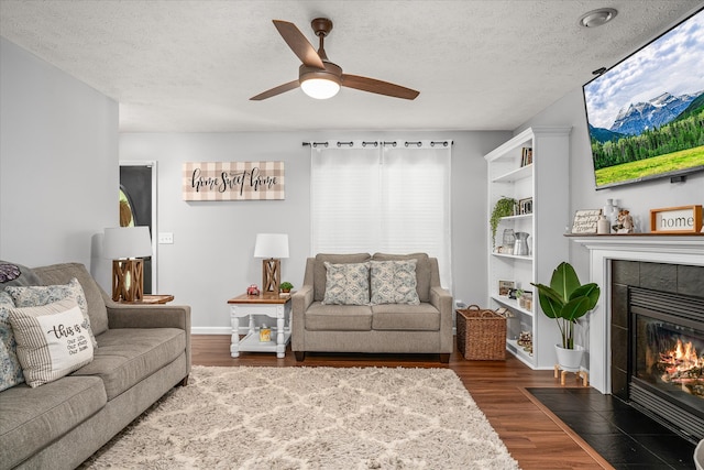 living room with ceiling fan, a tiled fireplace, dark hardwood / wood-style flooring, and a textured ceiling