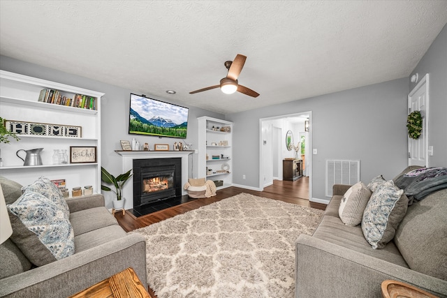 living room with a textured ceiling, dark wood-type flooring, and ceiling fan