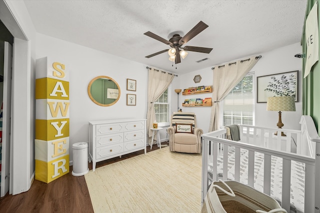 bedroom with a nursery area, hardwood / wood-style floors, ceiling fan, and a textured ceiling