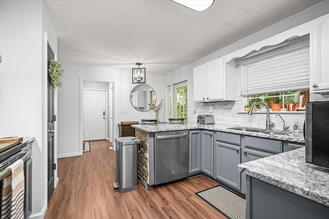 kitchen with stainless steel dishwasher, white cabinets, wood-type flooring, sink, and tasteful backsplash