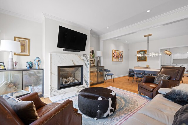 living room featuring an inviting chandelier, light hardwood / wood-style flooring, a fireplace, and crown molding