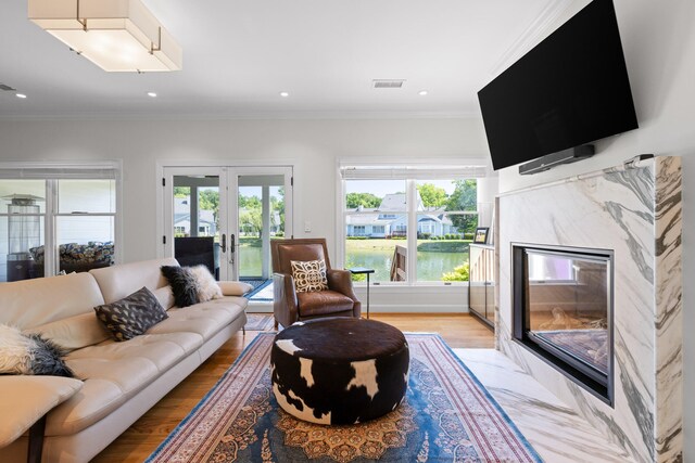 living room featuring a premium fireplace, ornamental molding, french doors, and light wood-type flooring