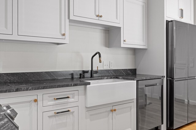 kitchen featuring stainless steel appliances, light wood-type flooring, dark stone countertops, sink, and white cabinetry