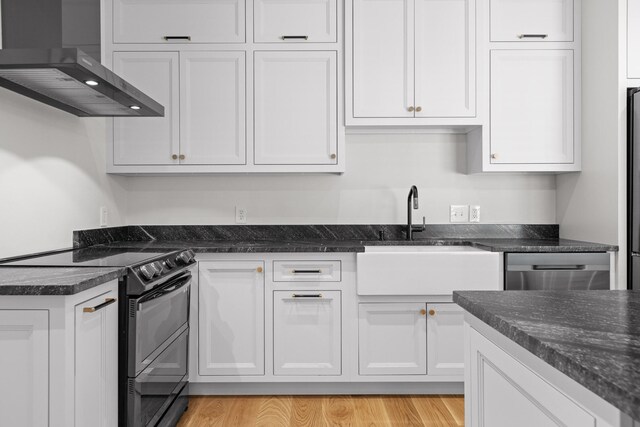 kitchen featuring wall chimney range hood, light hardwood / wood-style floors, white cabinets, black electric range oven, and sink