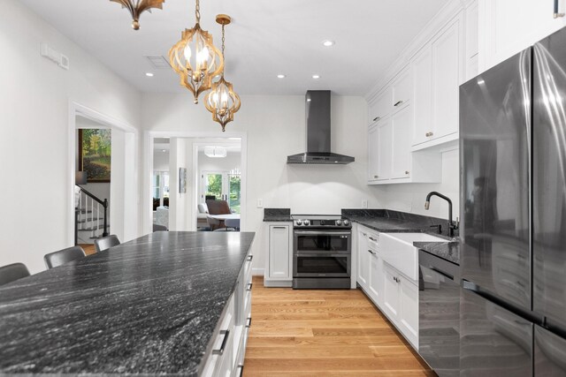 kitchen featuring light hardwood / wood-style flooring, decorative light fixtures, wall chimney exhaust hood, white cabinets, and appliances with stainless steel finishes