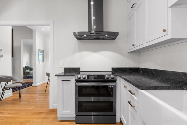 kitchen with fume extractor, light hardwood / wood-style flooring, double oven range, dark stone countertops, and white cabinets