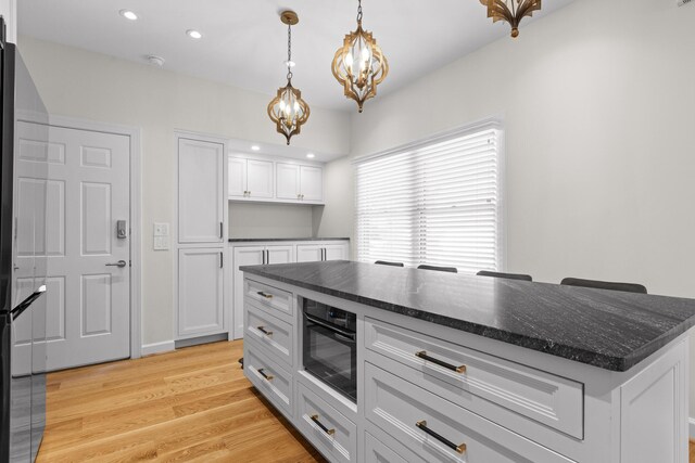 kitchen featuring a center island, white cabinetry, light hardwood / wood-style flooring, black oven, and pendant lighting